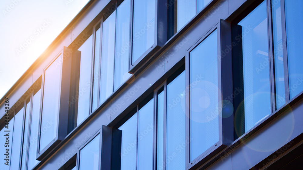 Obraz premium Modern glass building and rising sun. Glass facade on a bright sunny day with sunbeams in the blue sky. Economy, finances, business activity concept. 