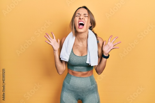 Obraz na plátne Beautiful hispanic woman wearing sportswear and towel celebrating mad and crazy for success with arms raised and closed eyes screaming excited