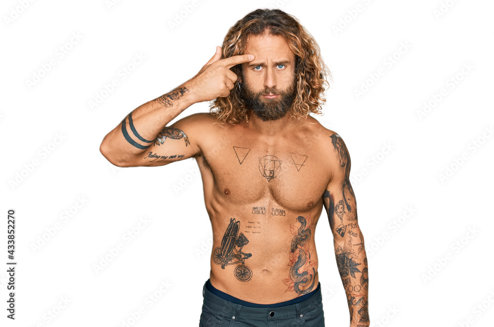 Fototapeta premium Handsome man with beard and long hair standing shirtless showing tattoos pointing unhappy to pimple on forehead, ugly infection of blackhead. acne and skin problem