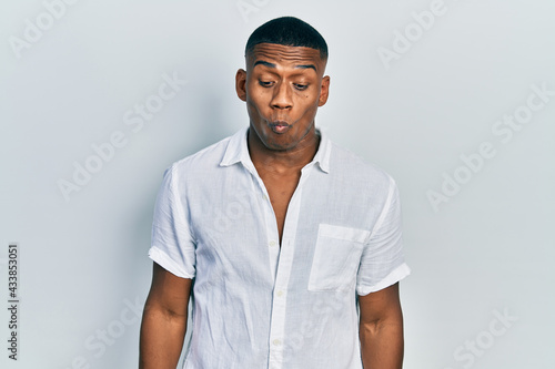 Young black man wearing casual white shirt making fish face with lips, crazy and comical gesture. funny expression.