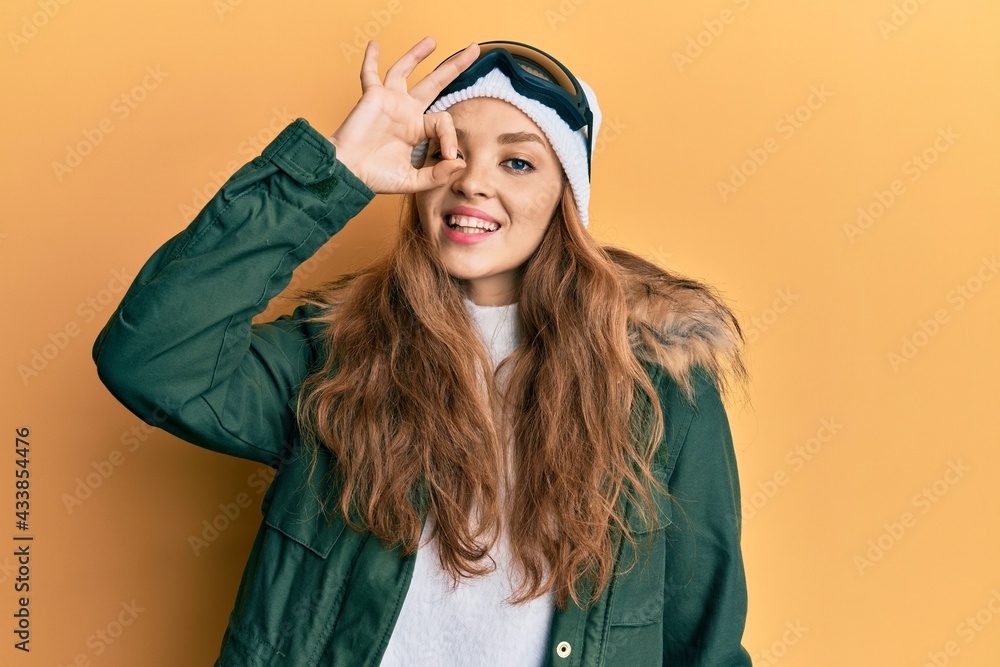 Beautiful blonde caucasian woman wearing snow wear and sky glasses smiling happy doing ok sign with hand on eye looking through fingers Beautiful blonde caucasian woman wearing snow wear and sky glasses smiling happy doing ok sign with hand on eye looking through fingers