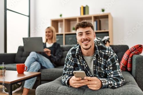 Young caucasian couple smiling happy using laptop and smartphone sitting on the sofa at home.