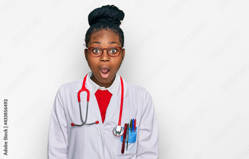 Young african american woman wearing doctor uniform and stethoscope afraid and shocked with surprise and amazed expression, fear and excited face.