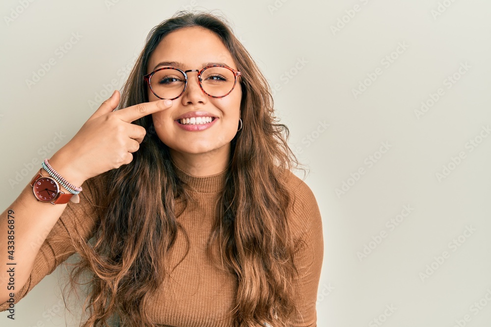 Young hispanic girl wearing casual clothes and glasses pointing with hand finger to face and nose, smiling cheerful. beauty concept Young hispanic girl wearing casual clothes and glasses pointing with hand finger to face and nose, smiling cheerful. beauty concept