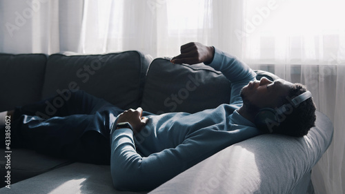 African American man wearing headphones listening to music. Lying on The Couch. High quality photo