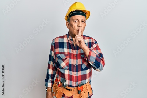 Senior hispanic man wearing handyman uniform asking to be quiet with finger on lips. silence and secret concept.