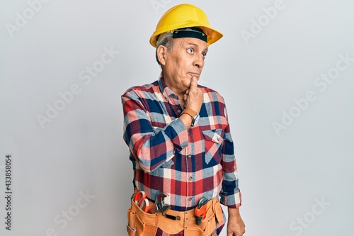 Senior hispanic man wearing handyman uniform with hand on chin thinking about question, pensive expression. smiling with thoughtful face. doubt concept.