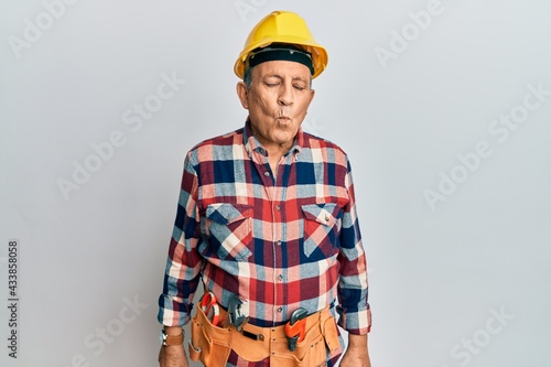 Senior hispanic man wearing handyman uniform making fish face with lips, crazy and comical gesture. funny expression.