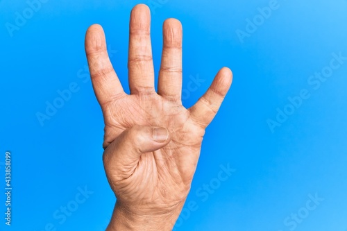 Hand of senior hispanic man over blue isolated background counting number 4 showing four fingers