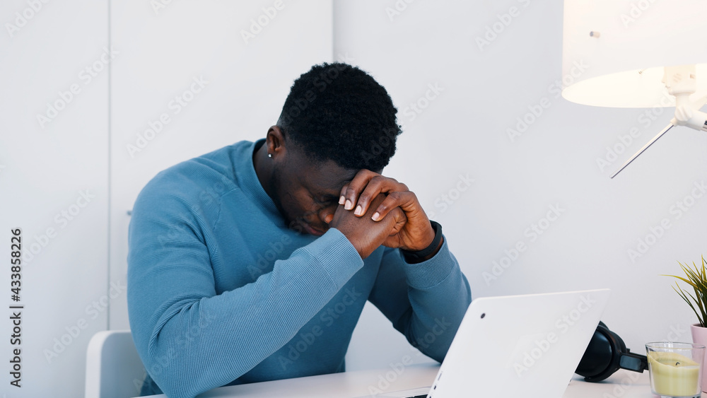 African American black man sitting at the table in front of a laptop working. Stressed out man working on his laptop. High quality photo African American black man sitting at the table in front of a laptop working. Stressed out man working on his laptop. High quality photo