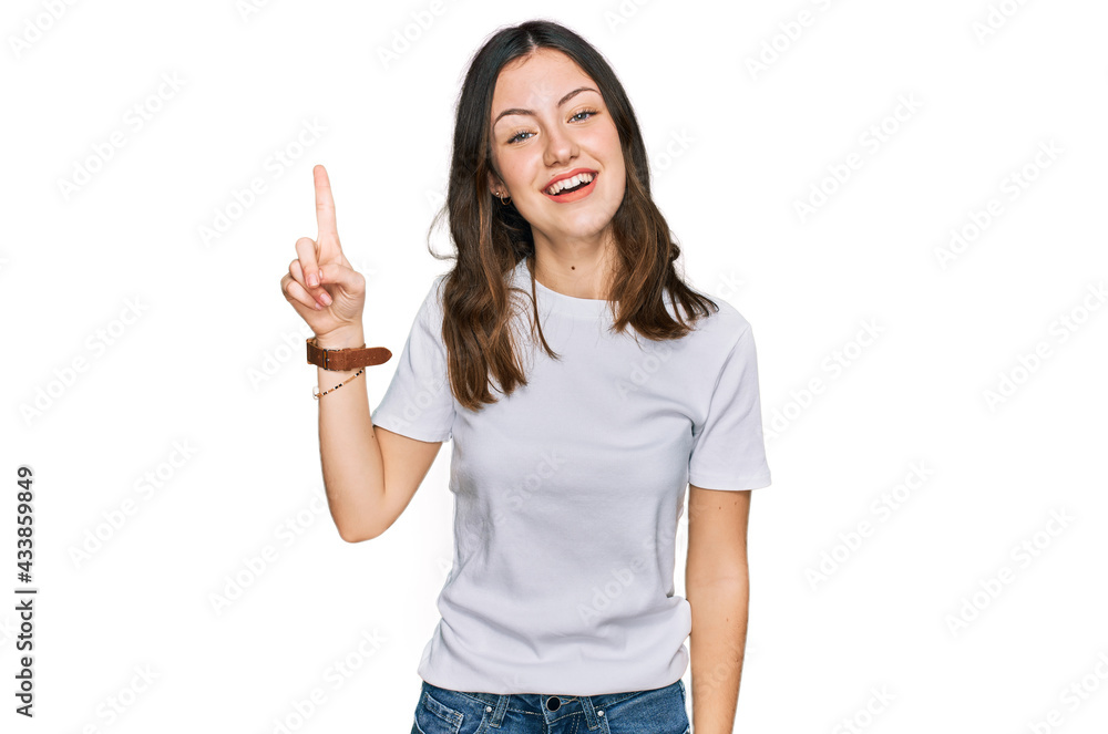 Young beautiful woman wearing casual white t shirt pointing finger up with successful idea. exited and happy. number one. Young beautiful woman wearing casual white t shirt pointing finger up with successful idea. exited and happy. number one.