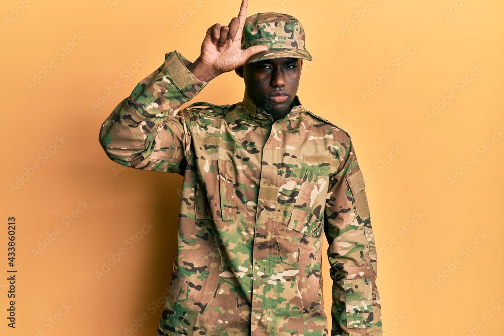 Fototapeta premium Young african american man wearing army uniform making fun of people with fingers on forehead doing loser gesture mocking and insulting.