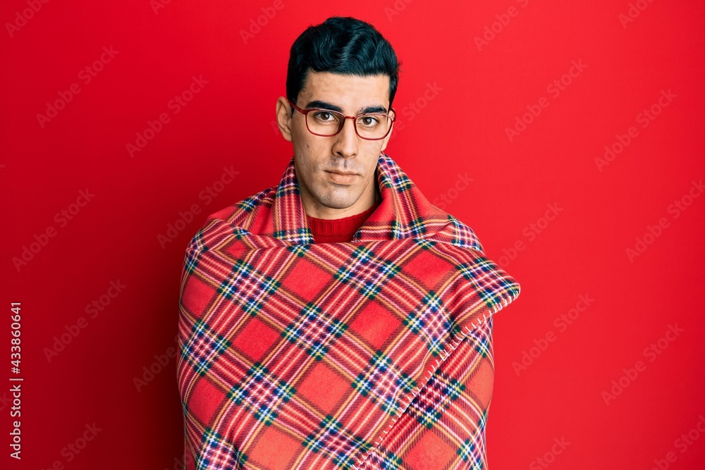 Handsome hispanic man wrapped in a red warm red blanket relaxed with serious expression on face. simple and natural looking at the camera. Handsome hispanic man wrapped in a red warm red blanket relaxed with serious expression on face. simple and natural looking at the camera.