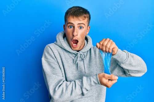 Young caucasian man holding slime afraid and shocked with surprise and amazed expression, fear and excited face.