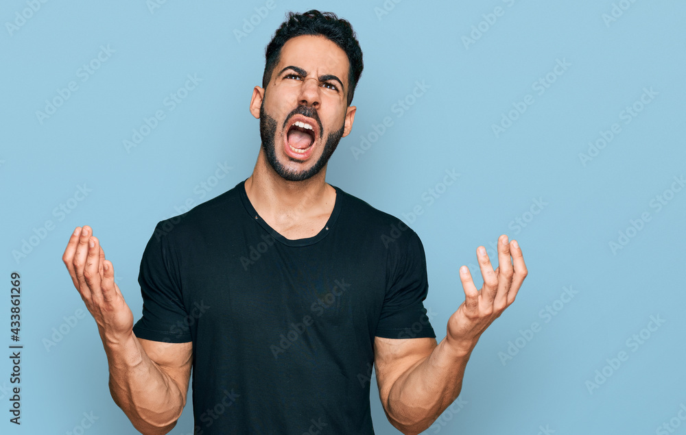 Hispanic man with beard wearing casual black t shirt crazy and mad shouting and yelling with aggressive expression and arms raised. frustration concept. Hispanic man with beard wearing casual black t shirt crazy and mad shouting and yelling with aggressive expression and arms raised. frustration concept.