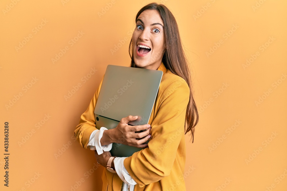 Young beautiful woman holding laptop celebrating crazy and amazed for success with open eyes screaming excited. Young beautiful woman holding laptop celebrating crazy and amazed for success with open eyes screaming excited.