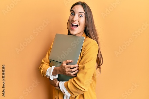 Young beautiful woman holding laptop celebrating crazy and amazed for success with open eyes screaming excited.