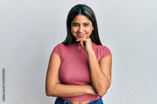 Young latin woman wearing casual clothes smiling looking confident at the camera with crossed arms and hand on chin. thinking positive.