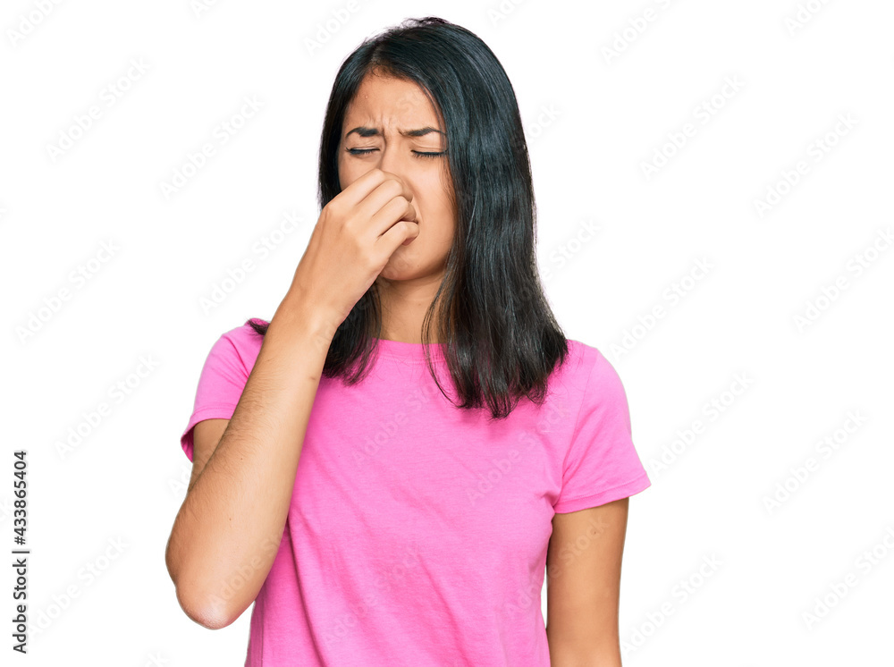 Beautiful asian young woman wearing casual pink t shirt smelling something stinky and disgusting, intolerable smell, holding breath with fingers on nose. bad smell Beautiful asian young woman wearing casual pink t shirt smelling something stinky and disgusting, intolerable smell, holding breath with fingers on nose. bad smell