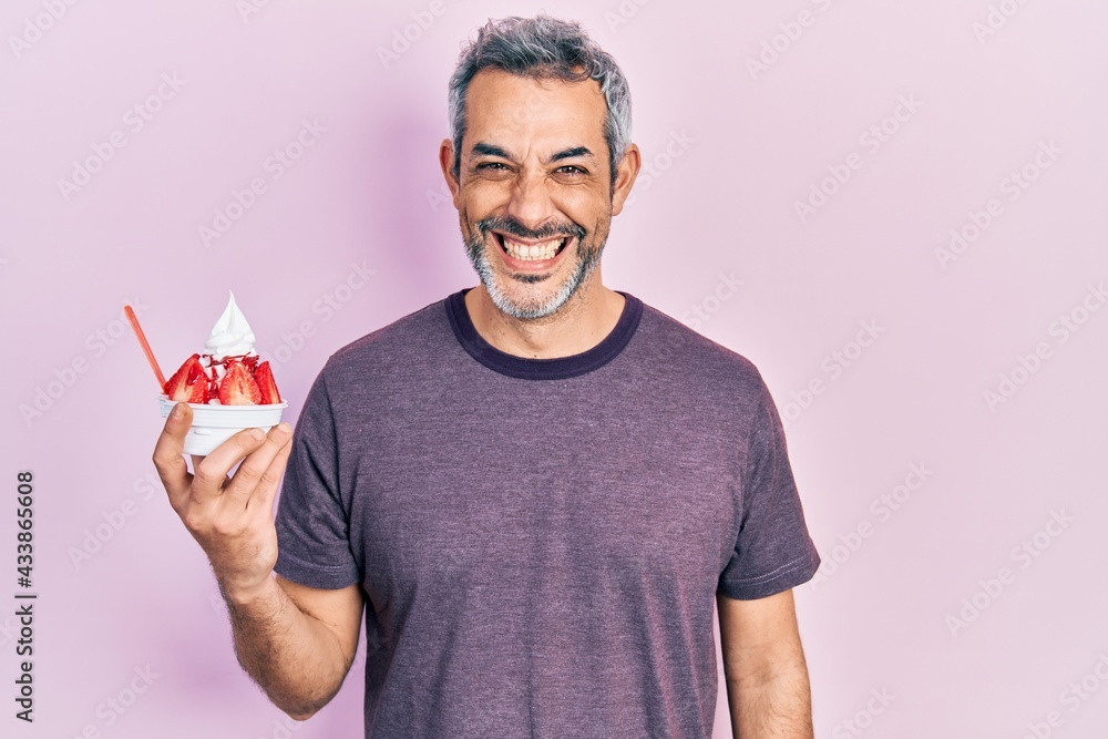 Handsome middle age man with grey hair eating strawberry ice cream