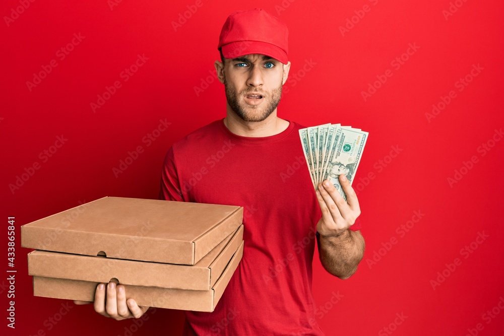 Young caucasian man holding take away food and 20 dollars in shock face, looking skeptical and sarcastic, surprised with open mouth Young caucasian man holding take away food and 20 dollars in shock face, looking skeptical and sarcastic, surprised with open mouth