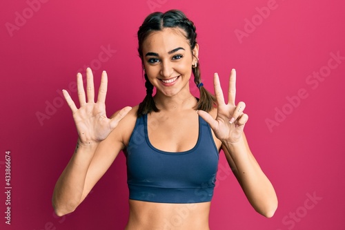 Young brunette girl wearing sportswear and braids showing and pointing up with fingers number eight while smiling confident and happy.