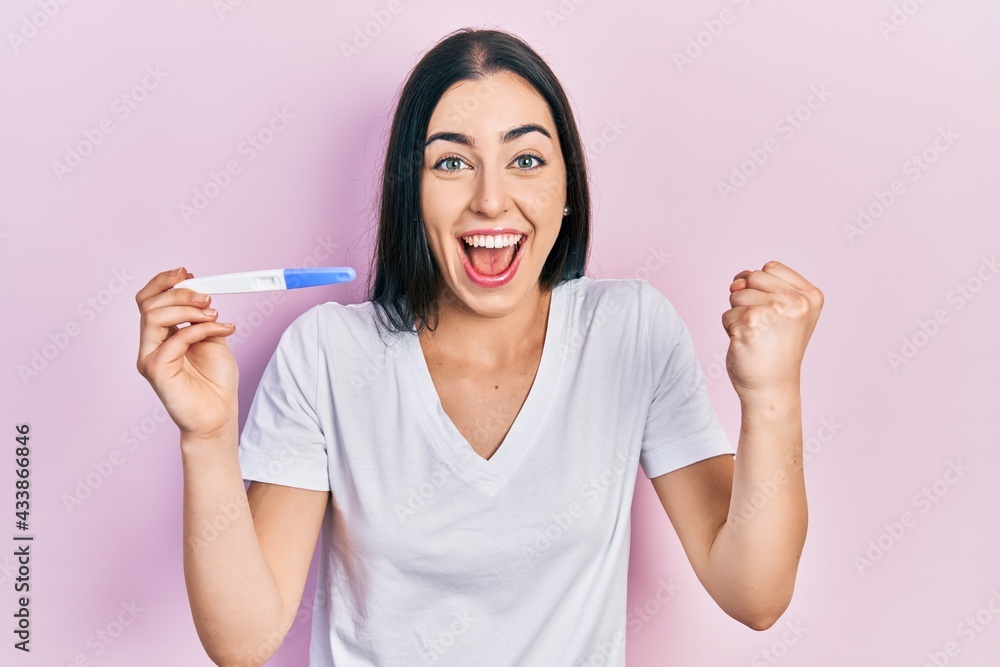 Beautiful woman with blue eyes holding pregnancy test result screaming proud, celebrating victory and success very excited with raised arms Beautiful woman with blue eyes holding pregnancy test result screaming proud, celebrating victory and success very excited with raised arms