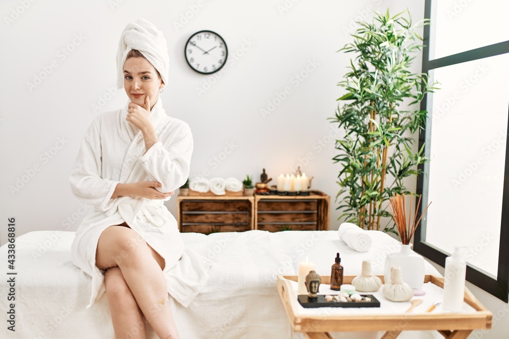 Young blonde woman wearing bathrobe at wellbeing spa looking confident at the camera smiling with crossed arms and hand raised on chin. thinking positive. Young blonde woman wearing bathrobe at wellbeing spa looking confident at the camera smiling with crossed arms and hand raised on chin. thinking positive.