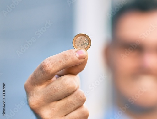Young hispanic businessman smiling happy holding 1 euro coin at the city.