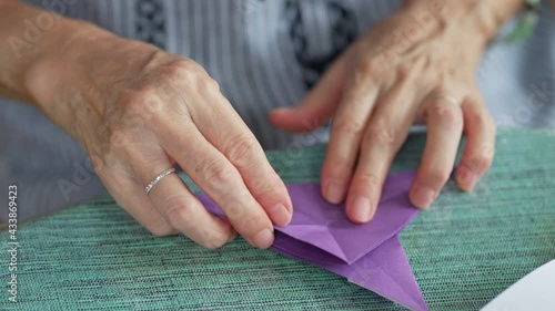 close up view of senior retired woman folding paper to make bird origami as a hobby at home