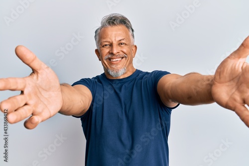 Middle age grey-haired man wearing casual clothes looking at the camera smiling with open arms for hug. cheerful expression embracing happiness.