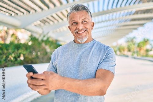 Middle age hispanic grey-haired man smiling happy using smartphone at the park.