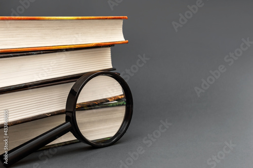 Magnifying glass and stack of books on black background. Space for text.