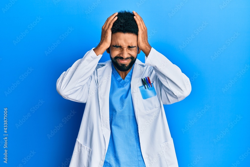 Handsome hispanic man with beard wearing doctor uniform suffering from headache desperate and stressed because pain and migraine. hands on head. Handsome hispanic man with beard wearing doctor uniform suffering from headache desperate and stressed because pain and migraine. hands on head.