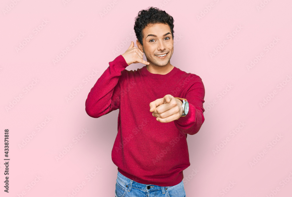 Young handsome man wearing casual clothes smiling doing talking on the telephone gesture and pointing to you. call me. Young handsome man wearing casual clothes smiling doing talking on the telephone gesture and pointing to you. call me.