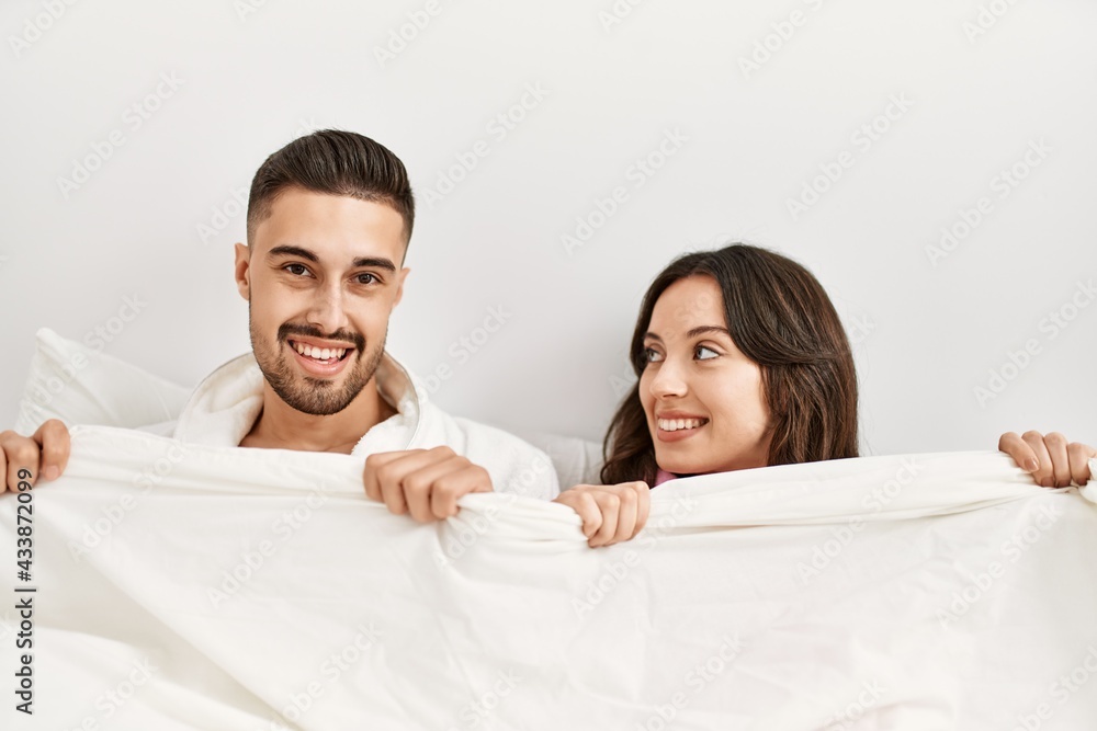 Young hispanic couple lying in bed and covering with bed sheet at home. Young hispanic couple lying in bed and covering with bed sheet at home.