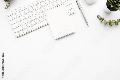 Small blank notebook with pen are on top of white office desk table with computer tools and supplies. Top view with copy space, flat lay.