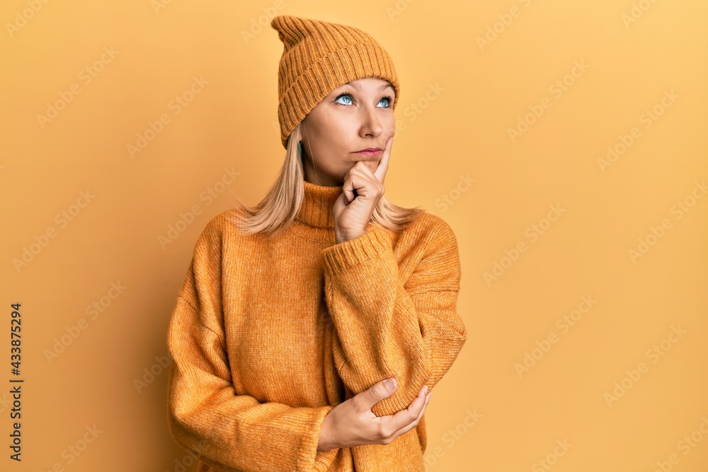 Fototapeta premium Middle age caucasian woman wearing wool winter sweater and hat serious face thinking about question with hand on chin, thoughtful about confusing idea