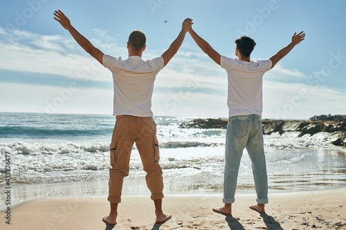 Young gay couple looking to the horizon breathing at the beach.