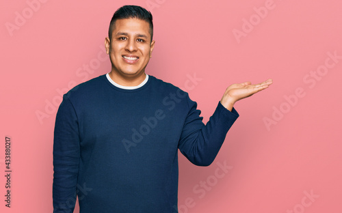 Young latin man wearing casual clothes smiling cheerful presenting and pointing with palm of hand looking at the camera.