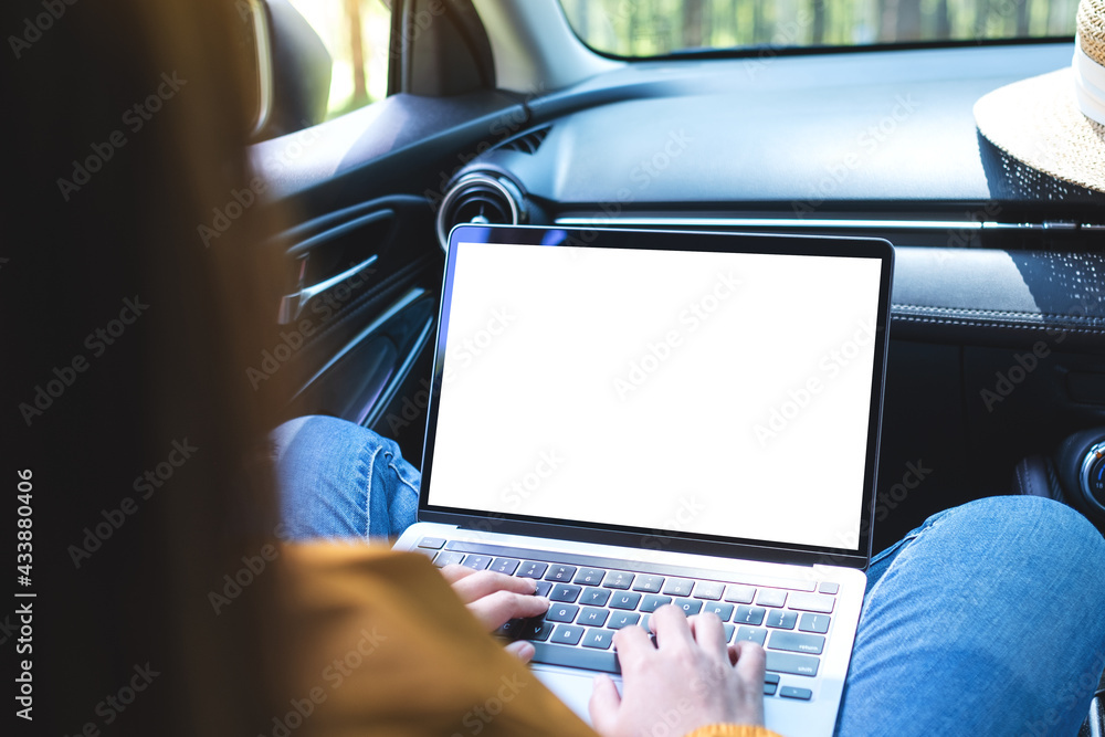 Mockup image of a woman using and typing on laptop computer with blank desktop screen in the car