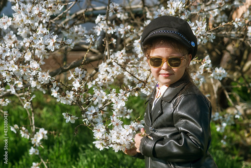 Fashionable little girl in a leather jacket near flowering plants