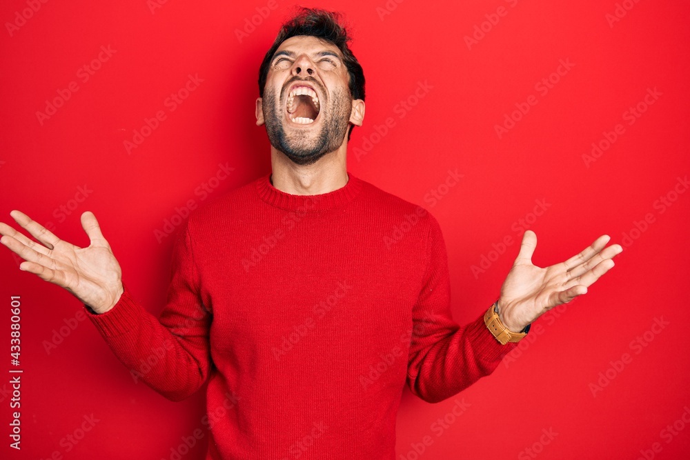 Handsome man with beard wearing casual red sweater crazy and mad shouting and yelling with aggressive expression and arms raised. frustration concept. Handsome man with beard wearing casual red sweater crazy and mad shouting and yelling with aggressive expression and arms raised. frustration concept.