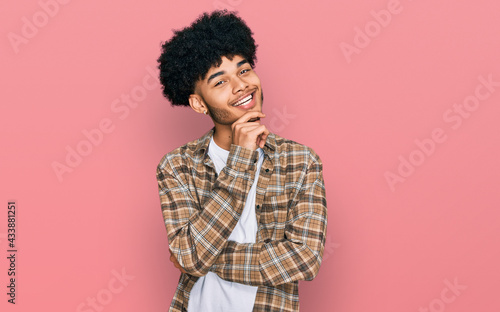 Young african american man with afro hair wearing casual clothes looking confident at the camera with smile with crossed arms and hand raised on chin. thinking positive. © Krakenimages.com