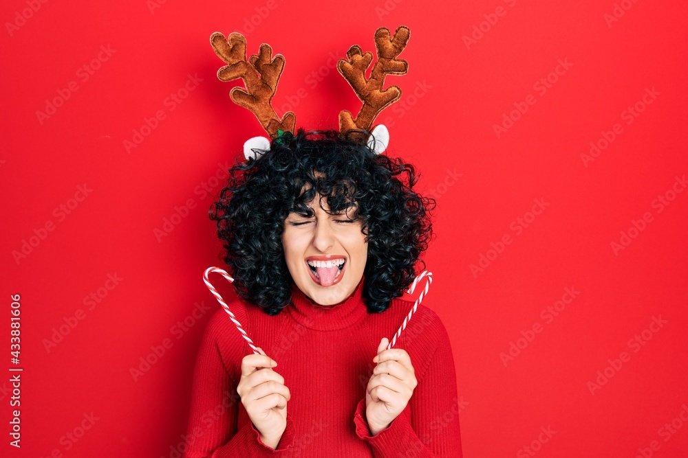 Young middle east woman wearing cute christmas reindeer horns sticking tongue out happy with funny expression. Young middle east woman wearing cute christmas reindeer horns sticking tongue out happy with funny expression.