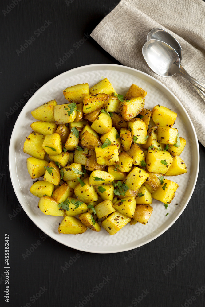 Homemade Roasted Potatoes with Mustard Seeds on a Plate on a black surface, top view. Flat lay, overhead, from above. Homemade Roasted Potatoes with Mustard Seeds on a Plate on a black surface, top view. Flat lay, overhead, from above.