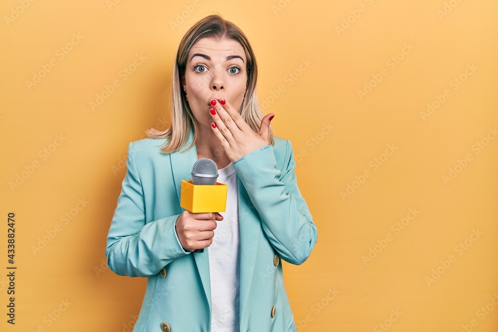 Beautiful caucasian woman holding reporter microphone covering mouth with hand, shocked and afraid for mistake. surprised expression Beautiful caucasian woman holding reporter microphone covering mouth with hand, shocked and afraid for mistake. surprised expression