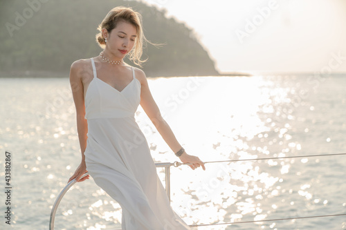 Woman wearing white dress relax on sailing yacht, romantic sunset.