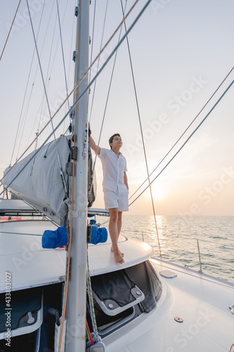 Man in white shirt standing on yacht looking at beautiful sunset.