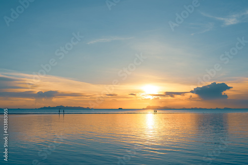 Silhouettes of people walking on the summer beach at sunset 